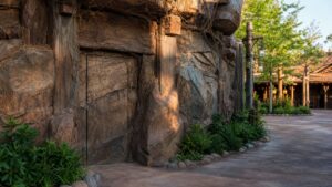 A realistic editorial image of a themed attraction facade with a concealed staff entrance blended into scenic rockwork.