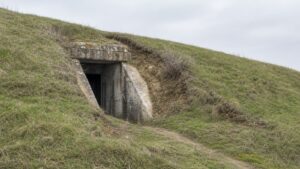 A realistic editorial image of a grass-covered bunker entrance partly hidden in a hillside.